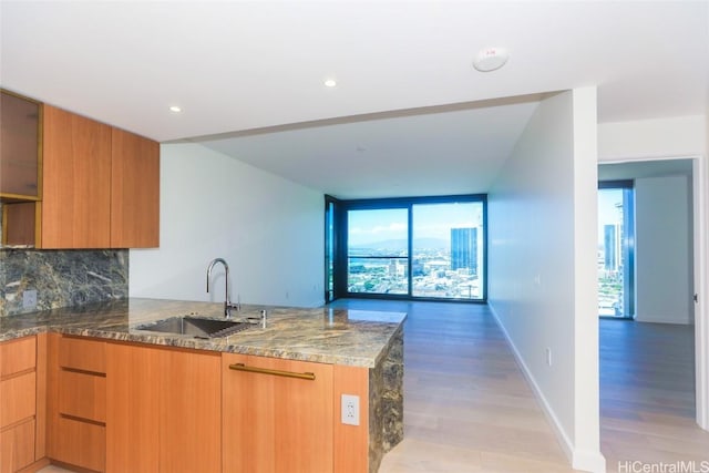 kitchen with sink, stone countertops, light wood-type flooring, kitchen peninsula, and decorative backsplash