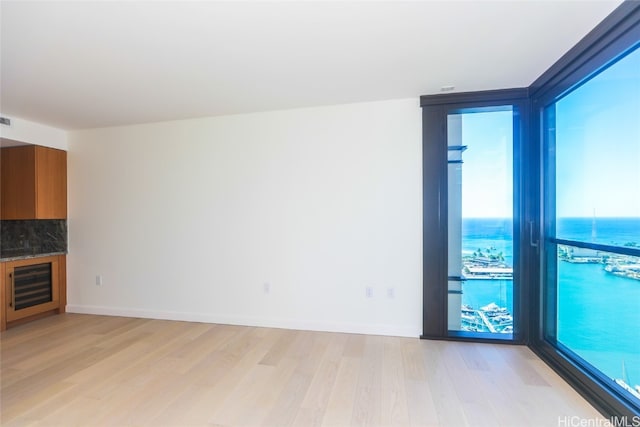 unfurnished living room with light hardwood / wood-style floors, a water view, and wine cooler