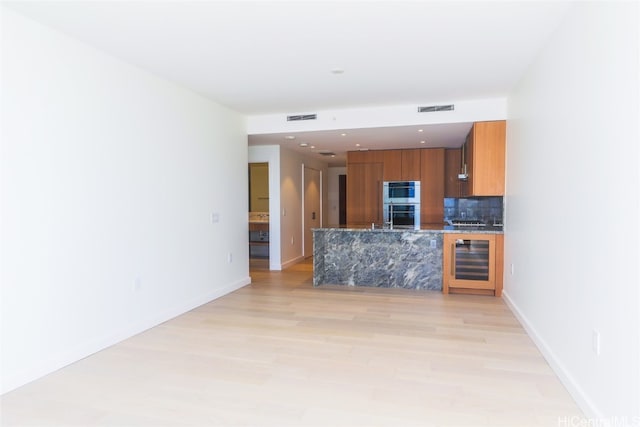 kitchen with double oven, decorative backsplash, wine cooler, and light hardwood / wood-style flooring