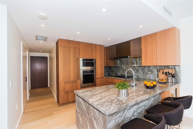 kitchen with double oven, light stone counters, a breakfast bar, backsplash, and kitchen peninsula