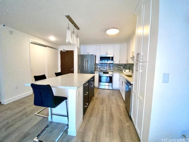 kitchen with a center island, white cabinets, decorative light fixtures, and appliances with stainless steel finishes