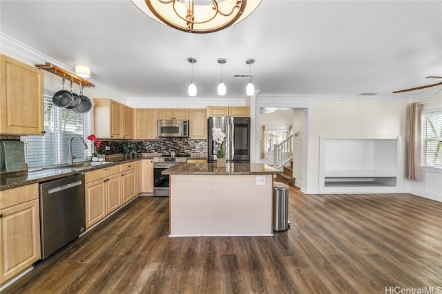 kitchen featuring sink, stainless steel appliances, a center island, decorative light fixtures, and dark stone counters