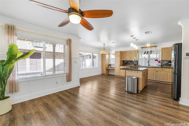 kitchen featuring crown molding, dark wood-type flooring, stainless steel refrigerator, hanging light fixtures, and a center island