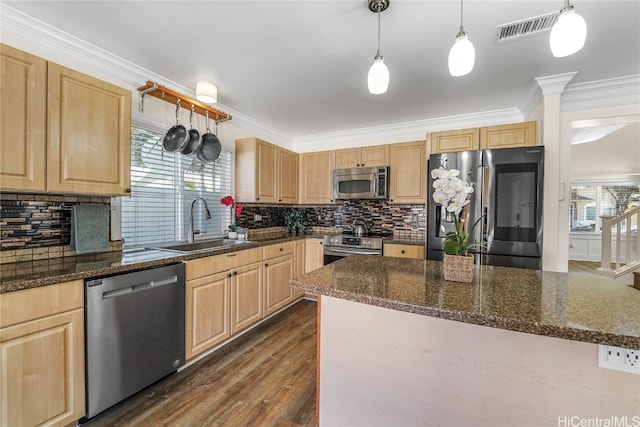 kitchen with appliances with stainless steel finishes, light brown cabinetry, decorative light fixtures, dark stone countertops, and ornamental molding