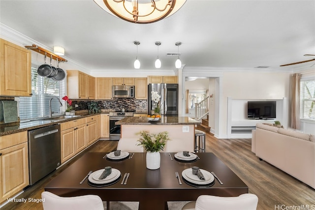 kitchen featuring sink, a center island, hanging light fixtures, dark stone countertops, and appliances with stainless steel finishes