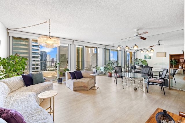 living room featuring ceiling fan with notable chandelier, a textured ceiling, and light hardwood / wood-style floors