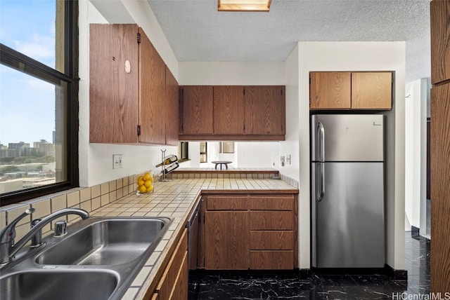 kitchen with stainless steel refrigerator, tile counters, sink, and a textured ceiling