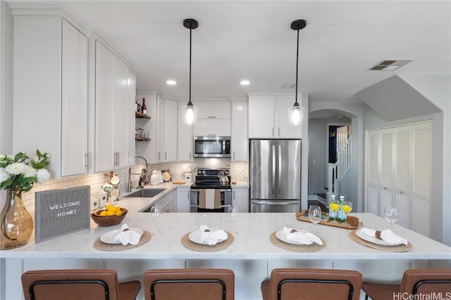 kitchen with sink, hanging light fixtures, appliances with stainless steel finishes, white cabinetry, and kitchen peninsula