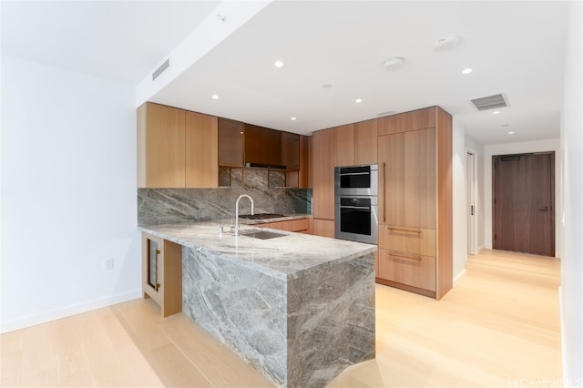 kitchen featuring sink, stainless steel double oven, tasteful backsplash, light hardwood / wood-style flooring, and kitchen peninsula