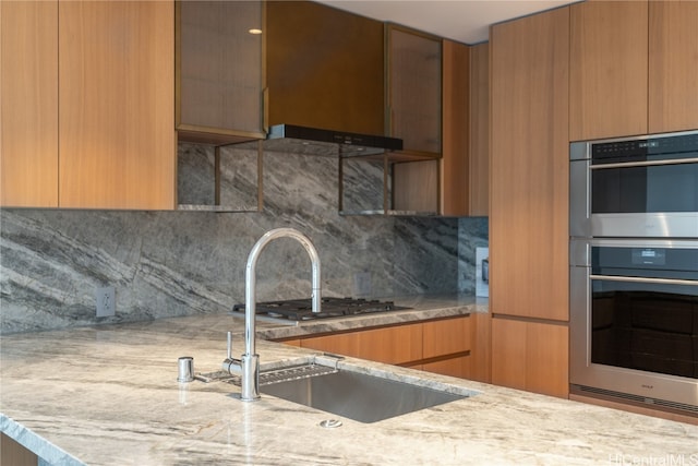 kitchen featuring light stone countertops, stainless steel double oven, tasteful backsplash, and sink