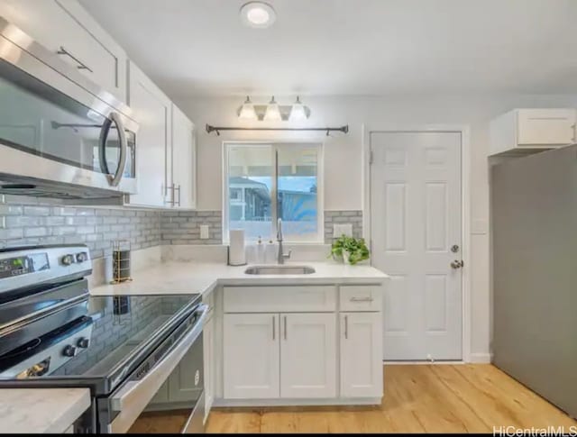 kitchen with light wood-type flooring, tasteful backsplash, stainless steel appliances, sink, and white cabinets