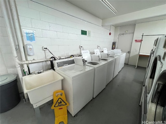 shared laundry area featuring separate washer and dryer, a sink, and concrete block wall