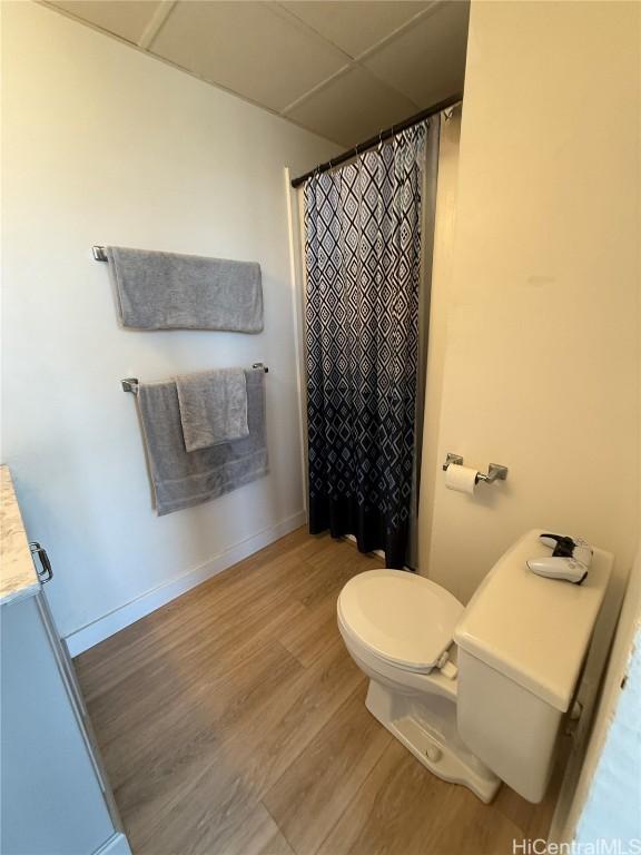 full bath with a paneled ceiling, a shower with shower curtain, toilet, wood finished floors, and baseboards