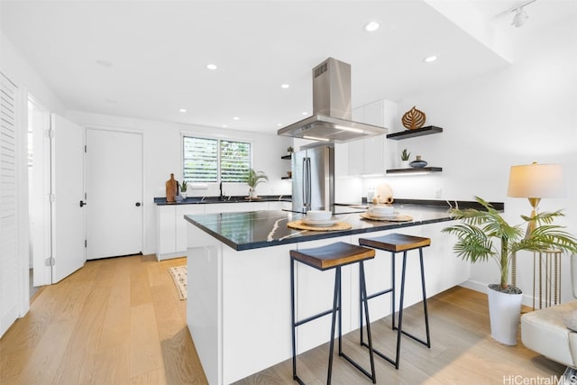 kitchen with white cabinets, a breakfast bar, island range hood, and light hardwood / wood-style floors