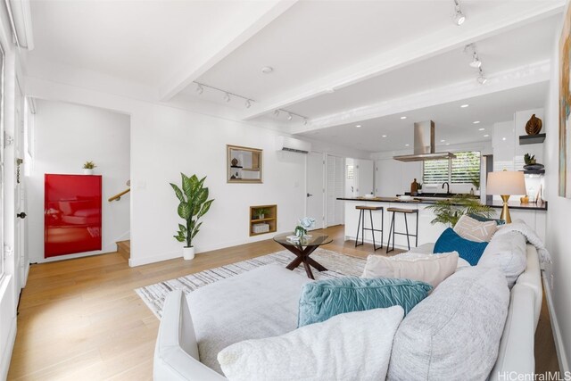 living room with beam ceiling, track lighting, light hardwood / wood-style floors, and an AC wall unit