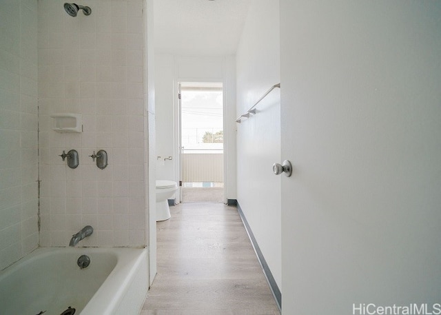 bathroom featuring hardwood / wood-style flooring, tiled shower / bath combo, and toilet