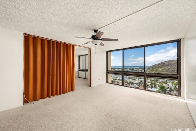 spare room featuring expansive windows, ceiling fan, a water view, and a textured ceiling