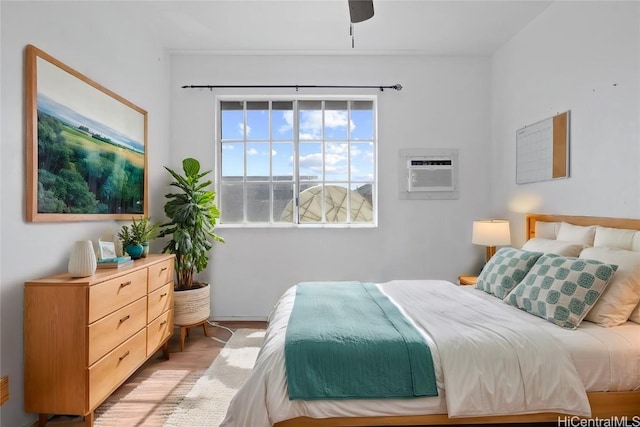 bedroom with ceiling fan, light wood-type flooring, and an AC wall unit