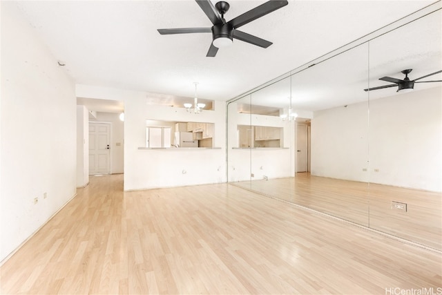 unfurnished living room featuring ceiling fan with notable chandelier and light hardwood / wood-style flooring