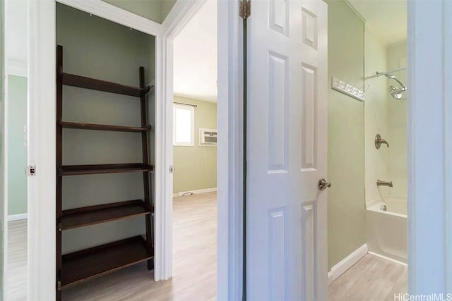 bathroom featuring bathing tub / shower combination, hardwood / wood-style floors, and an AC wall unit