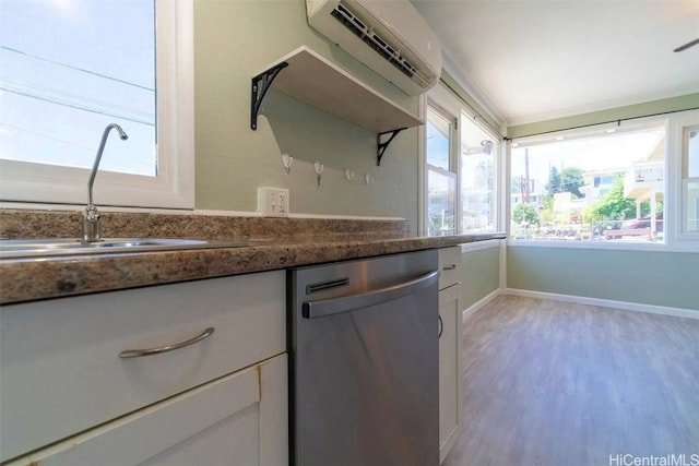 kitchen with light wood-type flooring, stainless steel dishwasher, a wall mounted AC, sink, and white cabinets