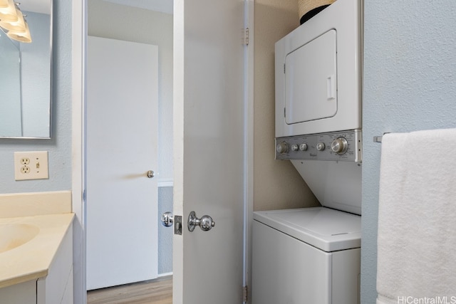 laundry area featuring stacked washing maching and dryer, light hardwood / wood-style flooring, and sink