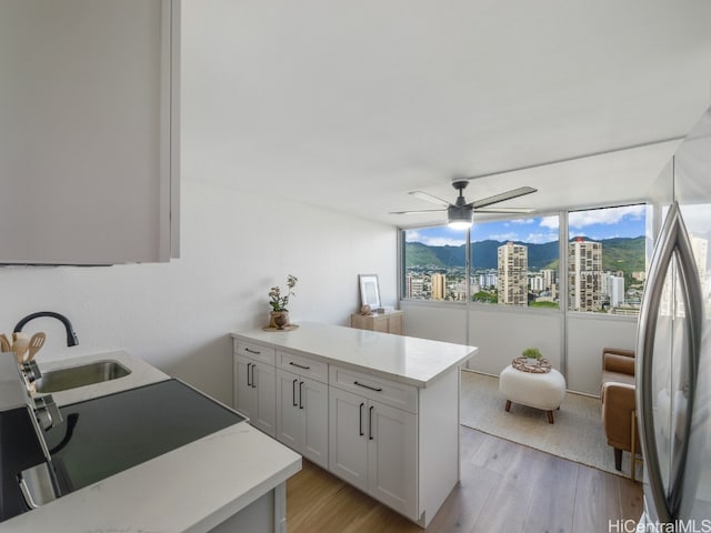 kitchen with sink, light hardwood / wood-style flooring, ceiling fan, a kitchen island, and white cabinetry