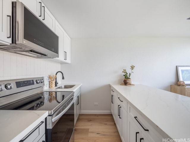 kitchen with appliances with stainless steel finishes, light stone counters, sink, light hardwood / wood-style flooring, and white cabinets