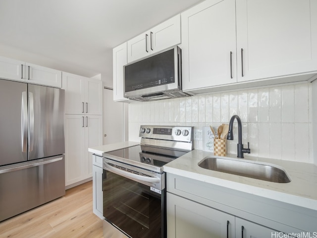 kitchen featuring sink, light hardwood / wood-style flooring, light stone countertops, appliances with stainless steel finishes, and white cabinetry