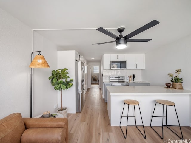 kitchen featuring backsplash, white cabinets, light wood-type flooring, appliances with stainless steel finishes, and kitchen peninsula