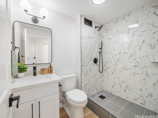 bathroom with hardwood / wood-style flooring, vanity, toilet, and a tile shower