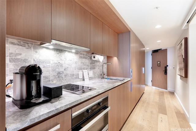 kitchen featuring light wood-type flooring, tasteful backsplash, stainless steel oven, sink, and range hood