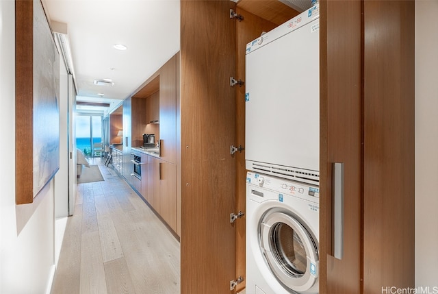 washroom with stacked washing maching and dryer and light hardwood / wood-style floors