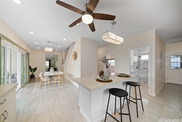 kitchen featuring a breakfast bar, a center island, white cabinets, ceiling fan with notable chandelier, and hanging light fixtures