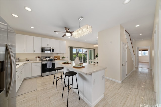 kitchen with white cabinets, hanging light fixtures, appliances with stainless steel finishes, a kitchen island, and a breakfast bar area