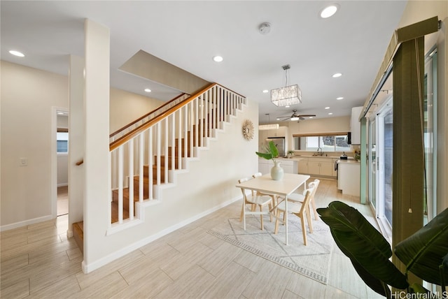 dining area with light wood-type flooring, ceiling fan with notable chandelier, and sink