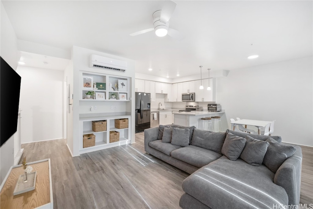 living room with an AC wall unit, ceiling fan, light hardwood / wood-style flooring, and sink