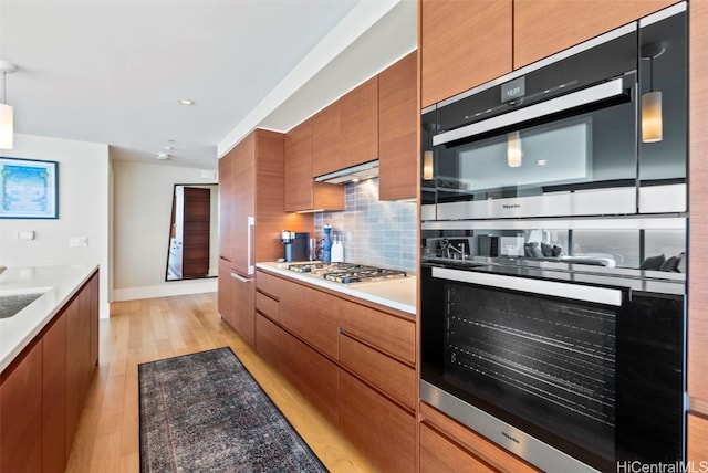 kitchen with stainless steel gas stovetop, tasteful backsplash, double oven, and light hardwood / wood-style flooring