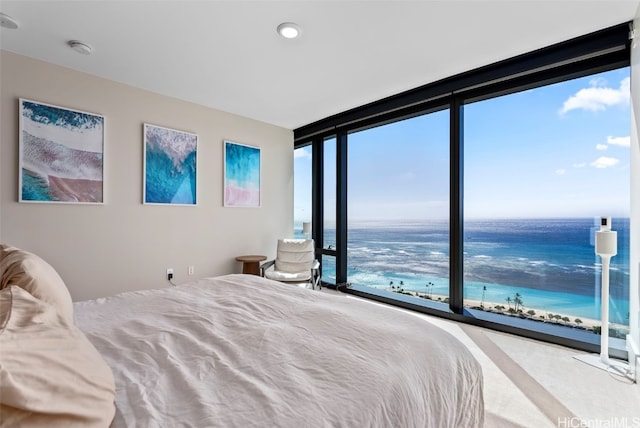 bedroom with multiple windows, a water view, a beach view, and a wall of windows