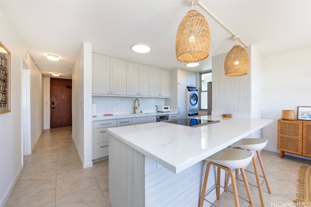 kitchen with stacked washing maching and dryer, black electric cooktop, a kitchen island, hanging light fixtures, and a breakfast bar area