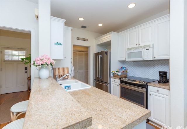 kitchen with a sink, backsplash, white cabinetry, appliances with stainless steel finishes, and light countertops