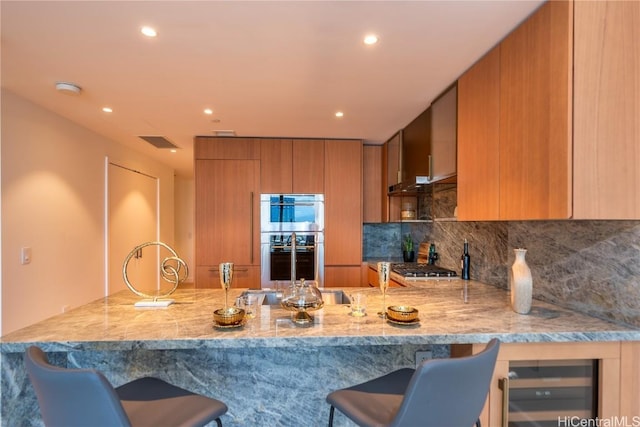 kitchen featuring a breakfast bar, tasteful backsplash, kitchen peninsula, stainless steel appliances, and light stone countertops