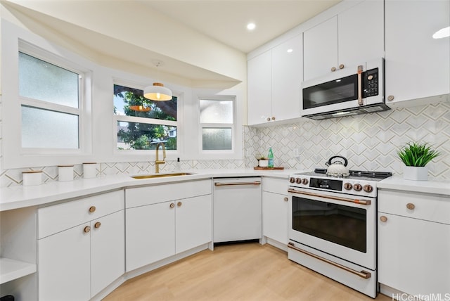 kitchen with white cabinets, sink, appliances with stainless steel finishes, decorative light fixtures, and light hardwood / wood-style floors