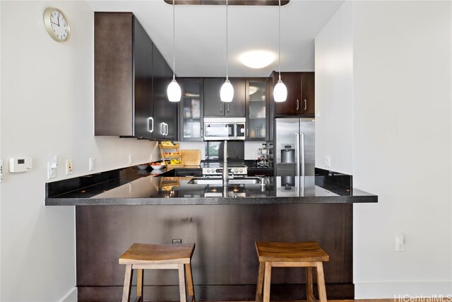 kitchen featuring kitchen peninsula, a kitchen breakfast bar, dark brown cabinets, stainless steel appliances, and decorative light fixtures