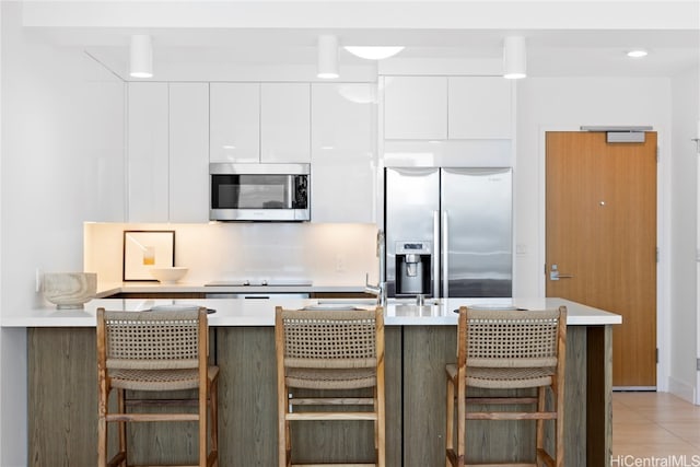 kitchen with a breakfast bar, white cabinets, stainless steel appliances, and light tile patterned floors