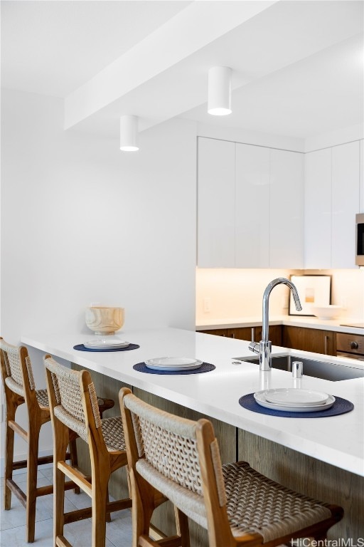 kitchen with a breakfast bar, sink, white cabinets, and light tile patterned floors