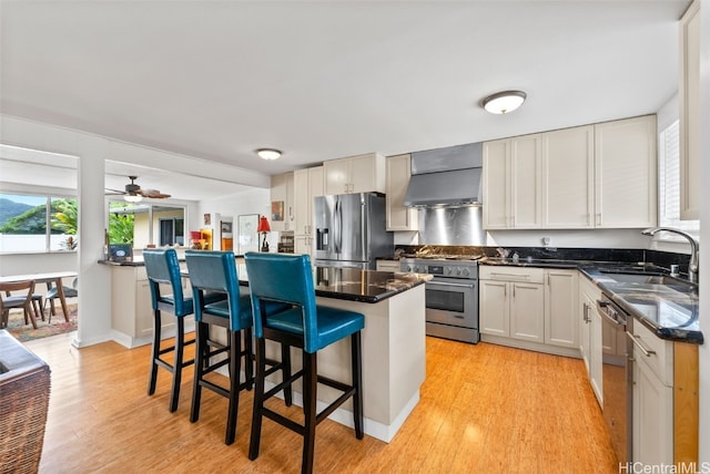 kitchen featuring sink, wall chimney range hood, a breakfast bar, stainless steel appliances, and white cabinets