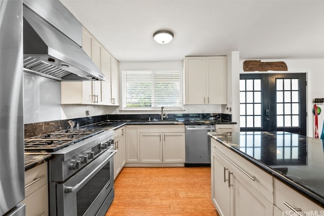 kitchen with french doors, white cabinets, wall chimney range hood, light hardwood / wood-style floors, and stainless steel appliances