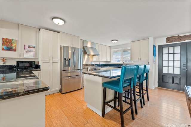 kitchen with white cabinetry, light hardwood / wood-style floors, wall chimney range hood, and appliances with stainless steel finishes