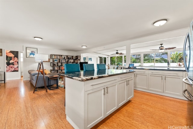 kitchen with stainless steel fridge, white cabinets, dark stone counters, a center island, and light hardwood / wood-style floors